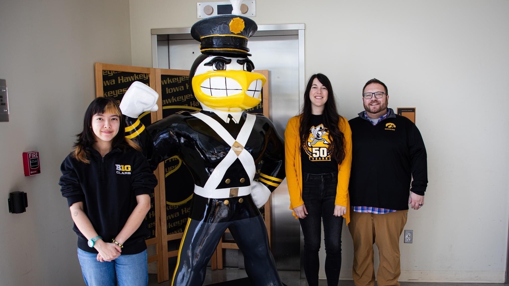 Artists Mae Dunning in black pull-over and jeans, Amanda Stout to Herky's right in yellow cardigan over the Alumni Band's 50th Anniversary t-shirt, and Marching Band Director Dr. Eric Bush in black pull over and khaki pants posing with the completed Alumni Band Herky for Herky on Parade. The Alumni Marching Herky is center, fully costumed in the original Marching Band Uniform from the 1940s and 50s.