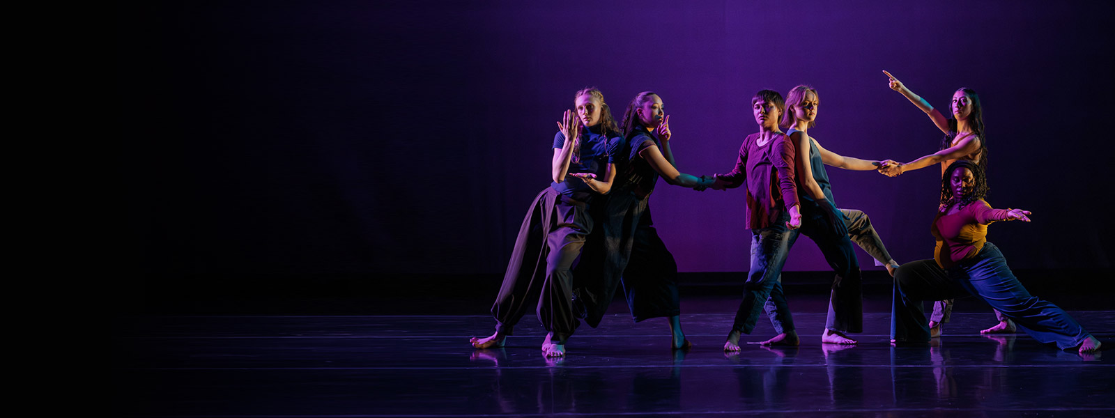 A group of UI Department of Dance students performing on stage under purple lighting
