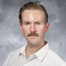 Photo of Colin DeJong from shoulders up, facing forward, white shirt, blond hair with mustache
