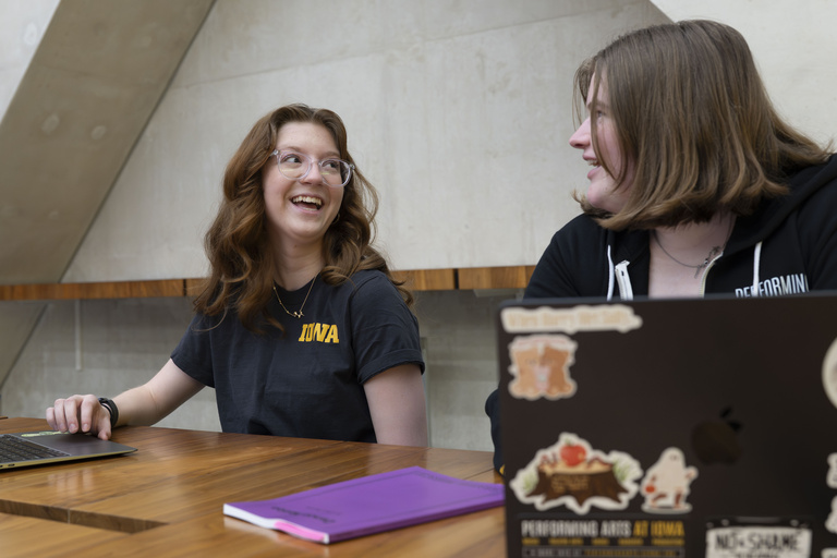 Two students laughing together wearing Performing Arts At Iowa merch