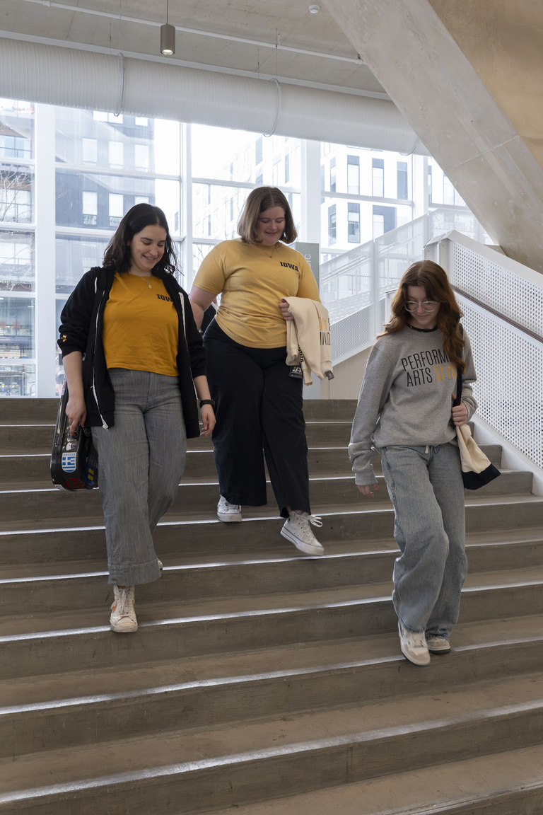 Three students wearing Performing Arts At Iowa merch walking down stairs