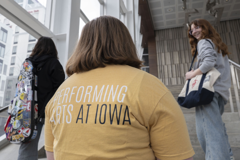 Three students walking up stairs, one wearing a light yellow Performing Arts At Iowa t-shirt