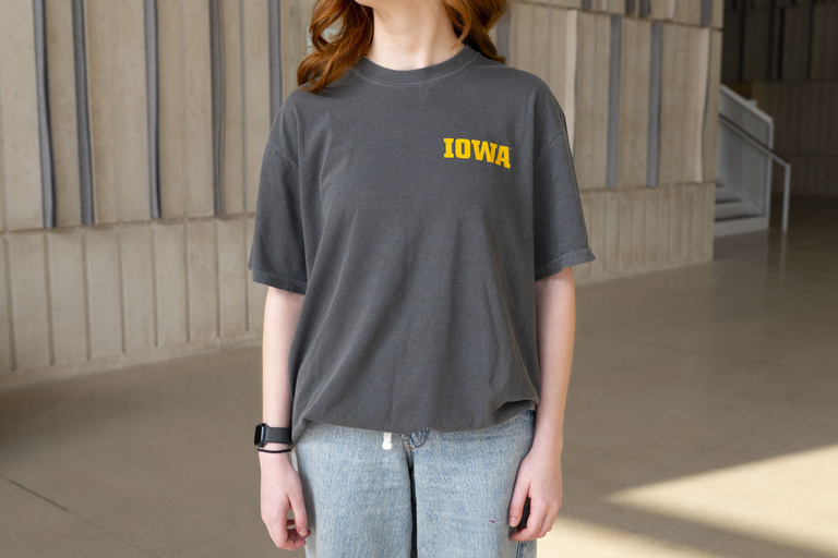 Student wearing a dark grey Performing Arts At Iowa t-shirt, showing the front