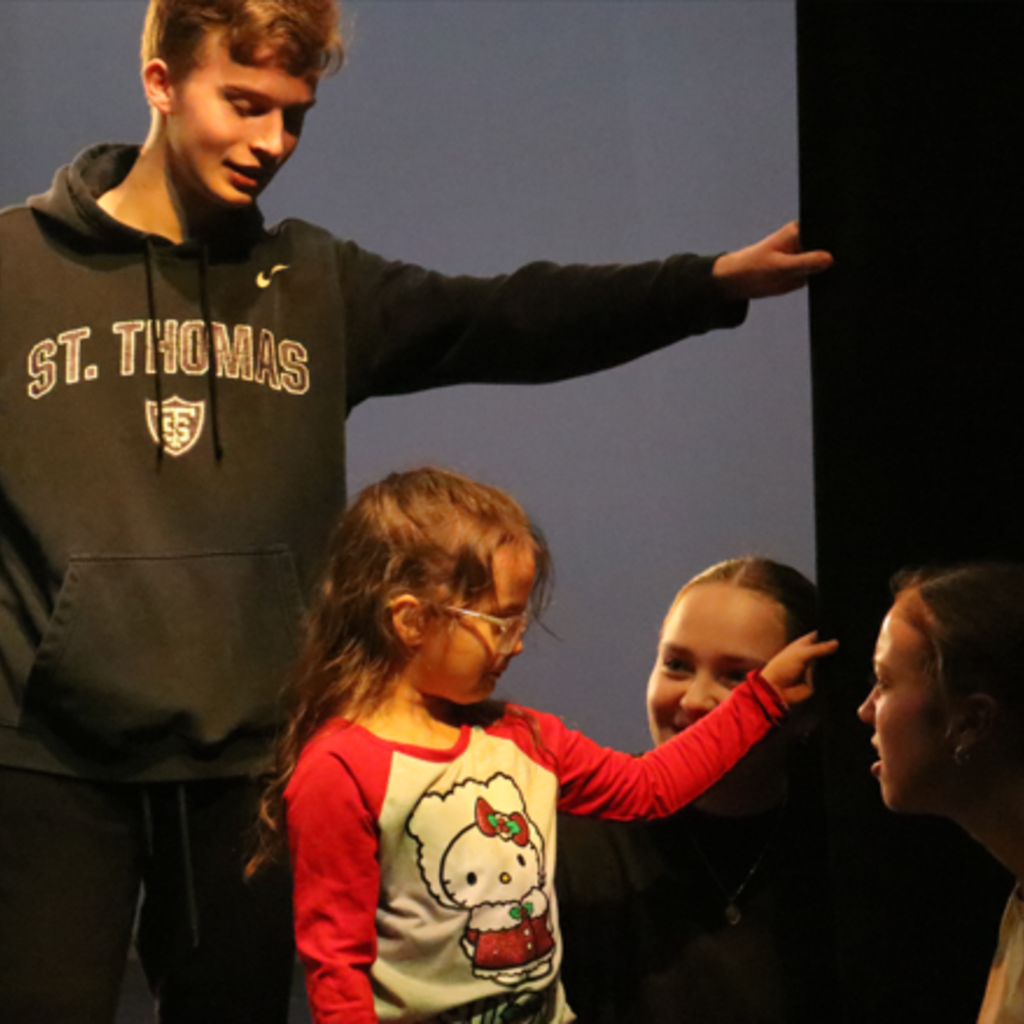 Six-year old EL student Jasmine, wearing a Hello Kitty shirt and pink glasses touches the black curtains in the Space Place theater as Jack Delaney (standing) and Ruby Gentzler and Madison Burkhart (kneeling) listen to Jasmine's description of the experience.
