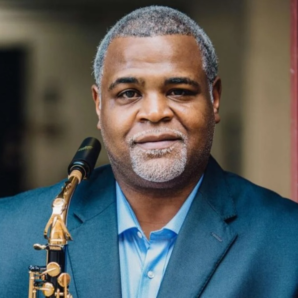 Professor Damani Phillips, wearing a blus shirt and blue suit coat and holding a black and gold saxophone